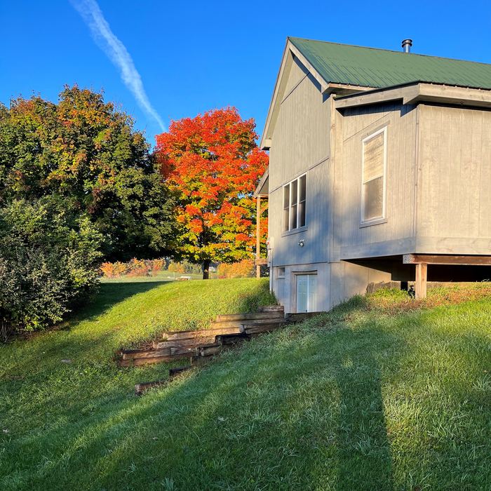 Side of the cabin with a bright red maple in autumn
